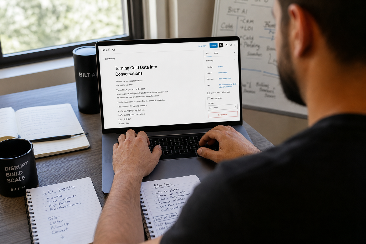over-the-shoulder view of a real estate investor writing a blog post on a laptop, notes scattered on desk, natural daylight through window