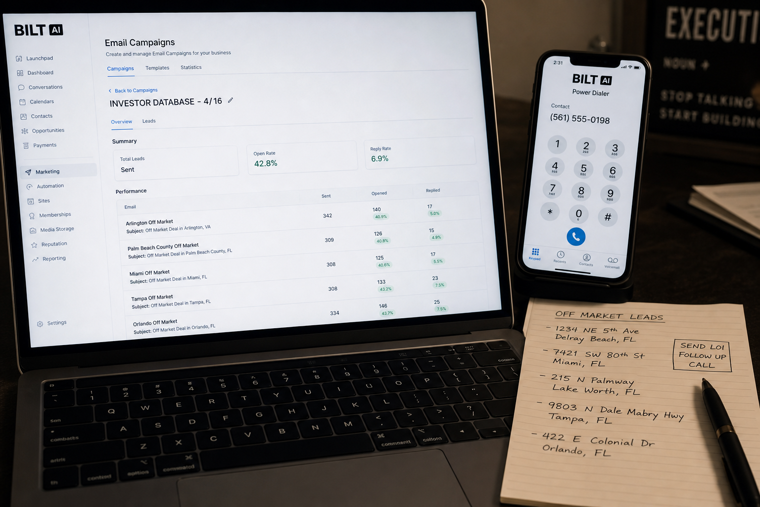 close-up of a laptop showing an email campaign report with open rates and reply columns, beside a smartphone with a dialer app open, handwritten notes with property addresses on paper
