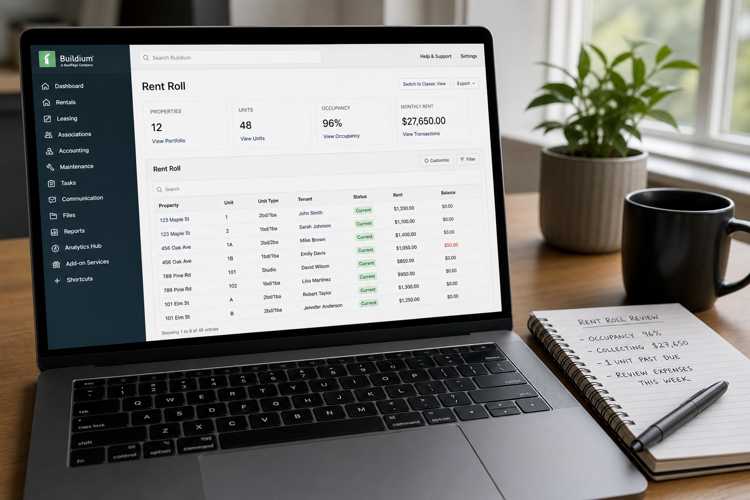 laptop screen displaying property management software dashboard with rent roll data, clean modern interface, desk setup with notebook and pen, natural daylight